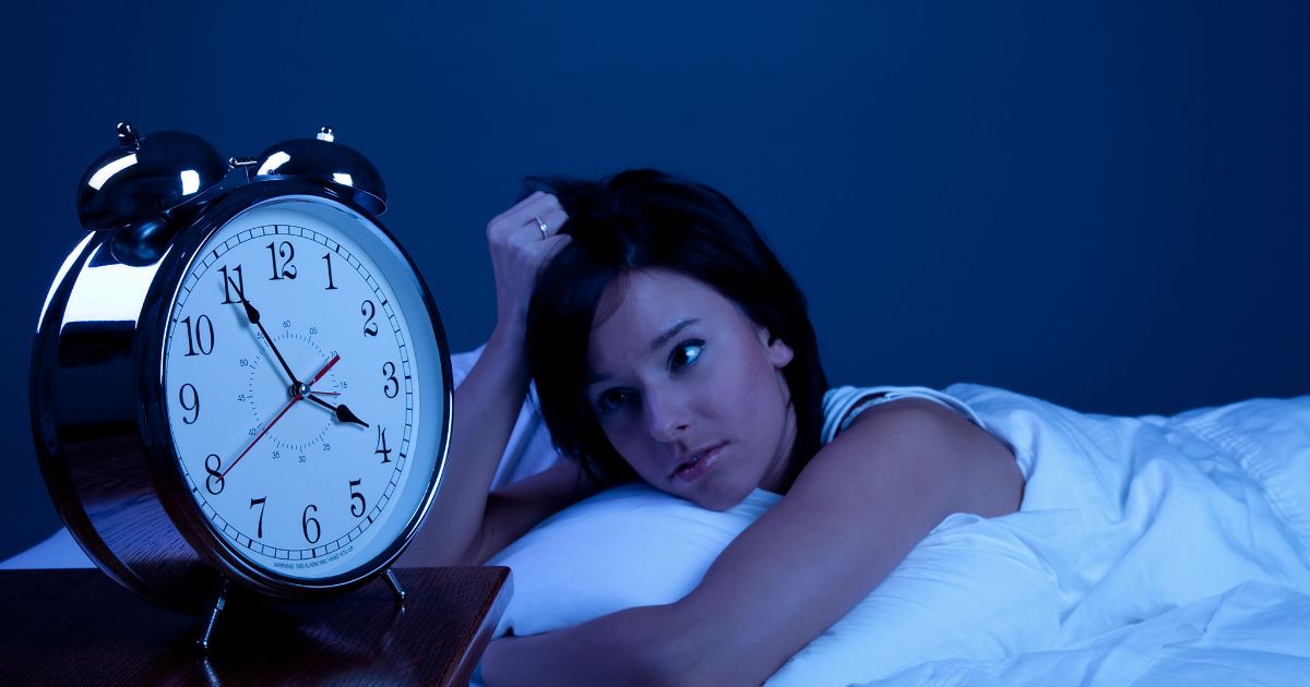 woman in bed looking tiredly at clock