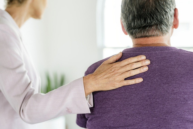 woman's hand on man's back for support